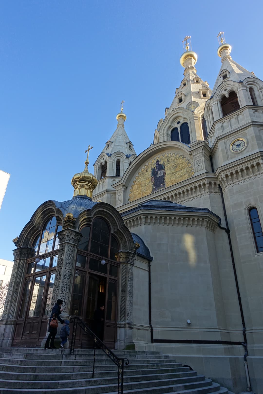 Low-angle view of the entrance porch, mosaic, and golden onion domes.