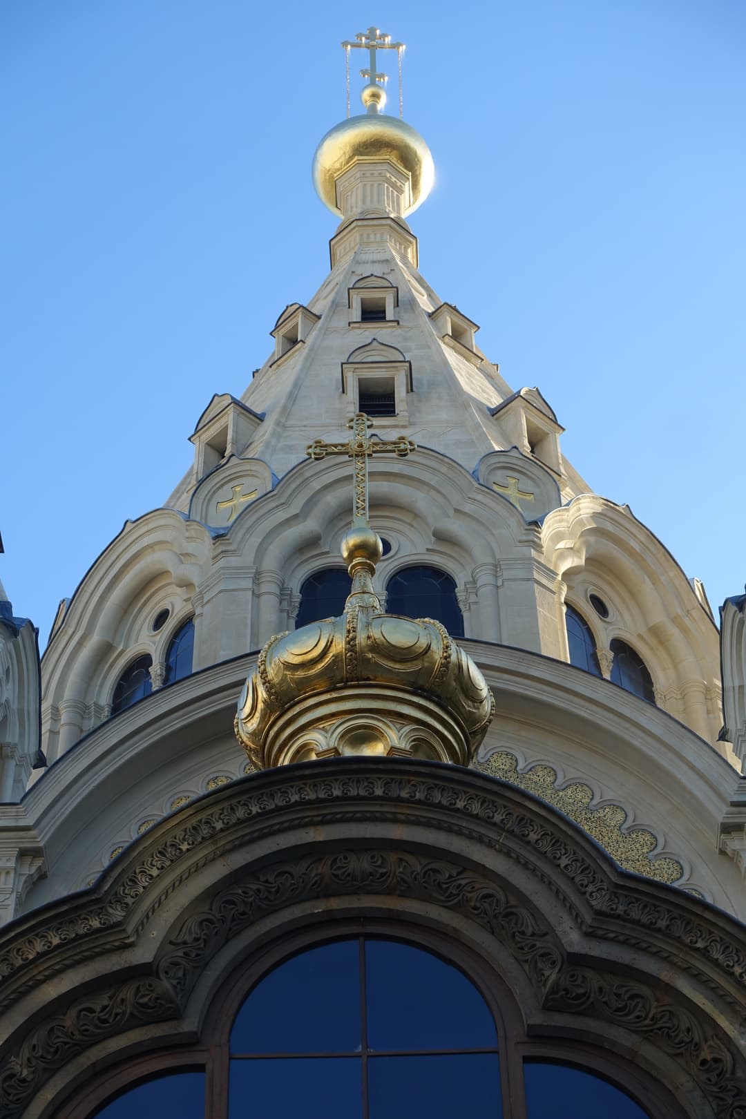 Low-angle view of the golden domes and tented spire against a clear blue sky.