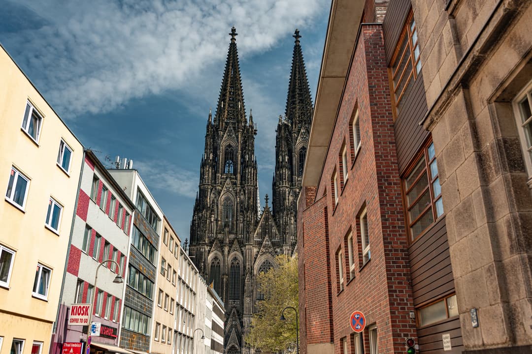 Twin spires of Cologne Cathedral framed by modern city buildings.