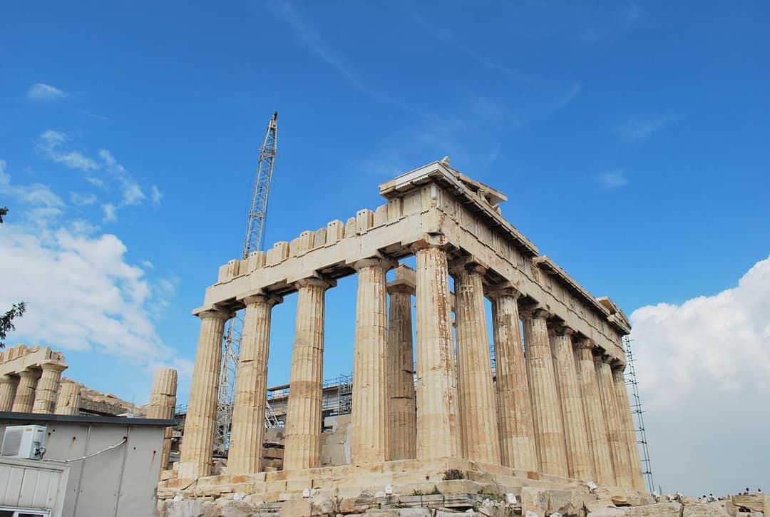 Low-angle view of the Parthenon colonnade under restoration in daylight.