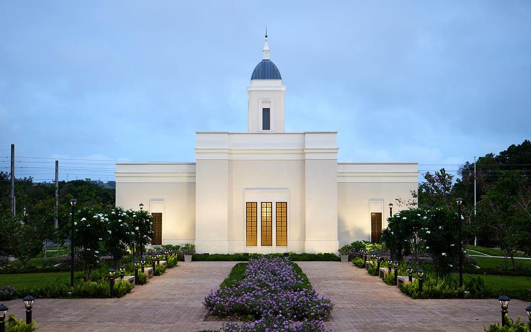 Front exterior view of the Yigo Guam Temple at dusk with a garden walkway.