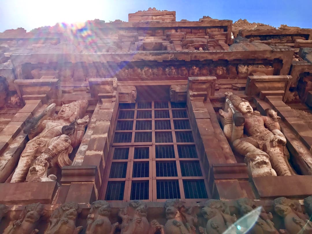 Low-angle view of dvarapala statues beside a stone window in sunlight