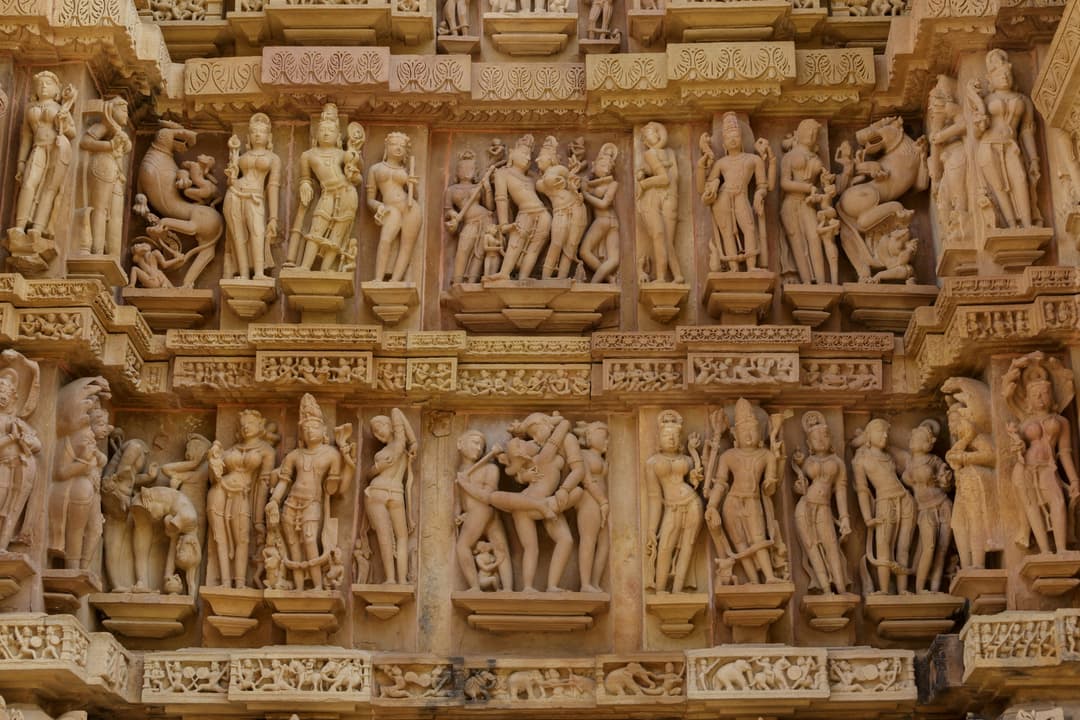 Detailed erotic and divine sandstone reliefs on the exterior temple wall.