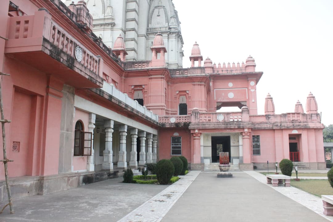 Paved courtyard and pink colonnaded facade beneath the temple shikhara.