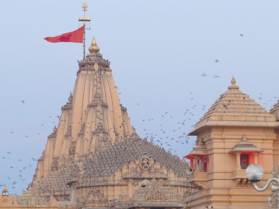 The shikhara and fluttering flag of Somnath Temple with birds in flight.