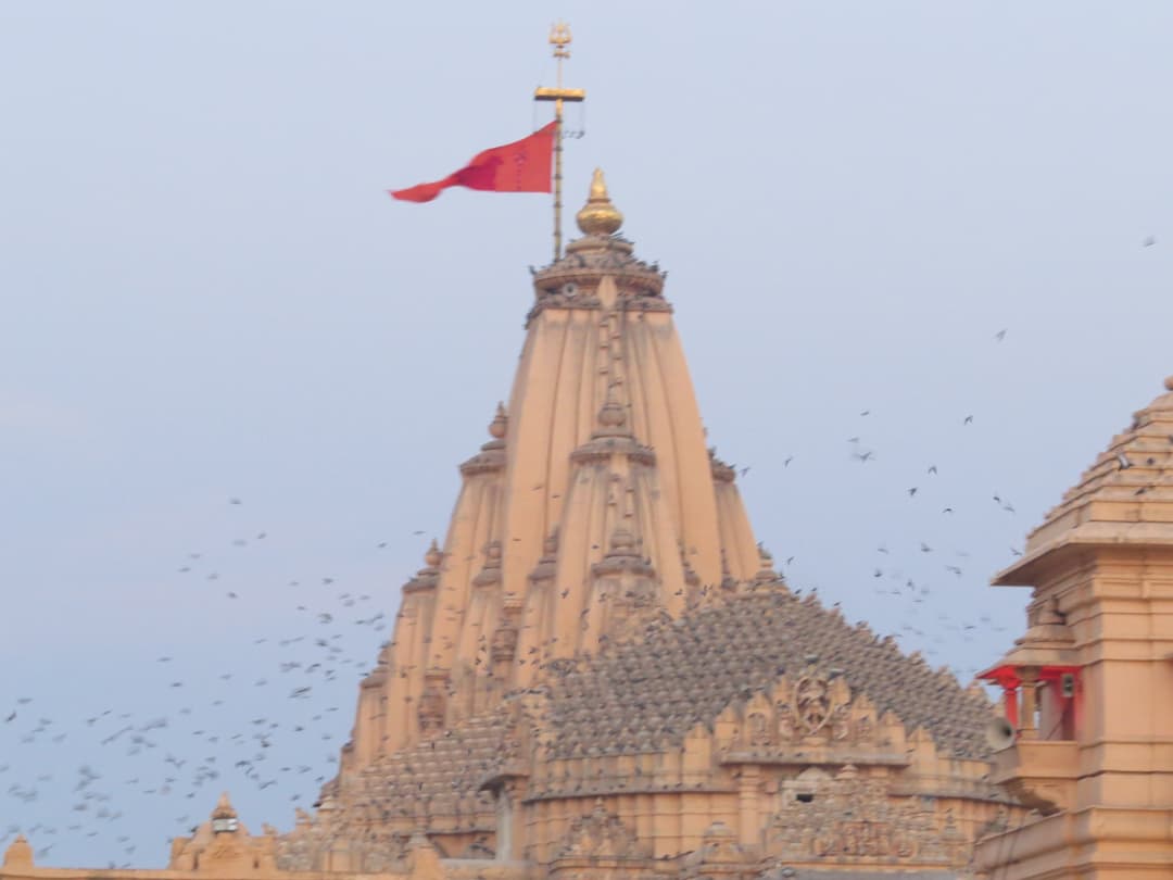The main shikhara and flag of Somnath Temple with birds in flight