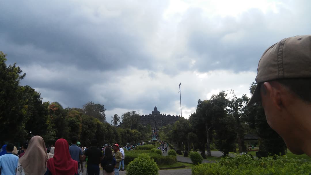 Distant view of Borobudur from the park pathway under an overcast sky.