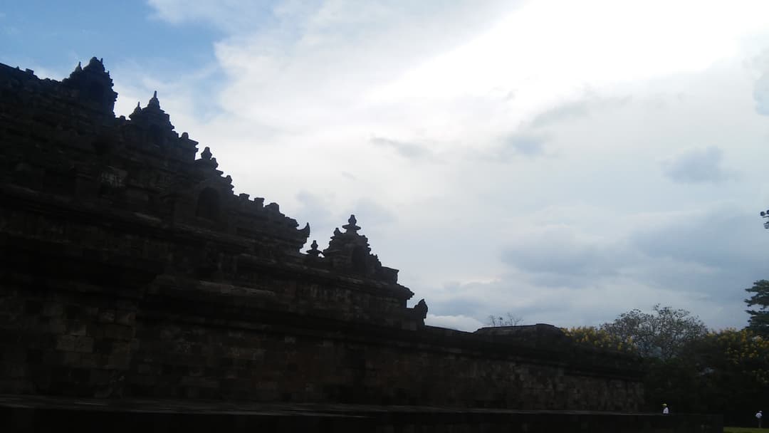 Mur du temple de Borobudur et flèches étagées sur fond de ciel nuageux.