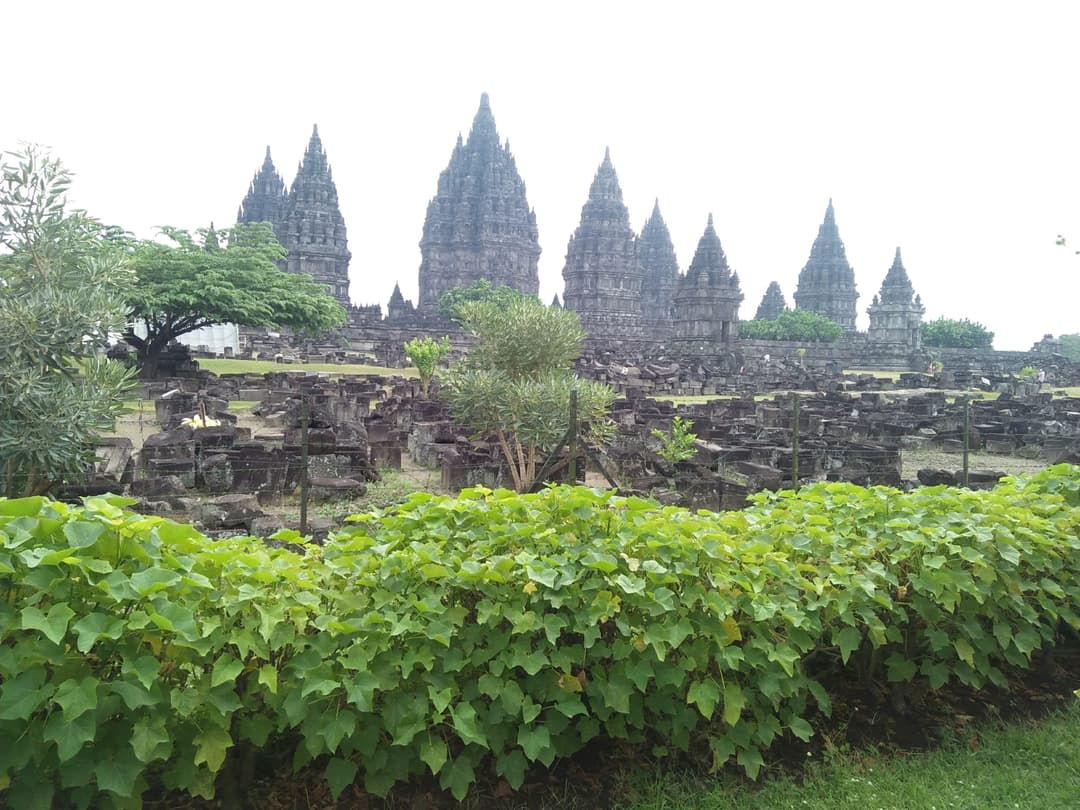 Prambanan temple spires viewed across scattered stone ruins and gardens.