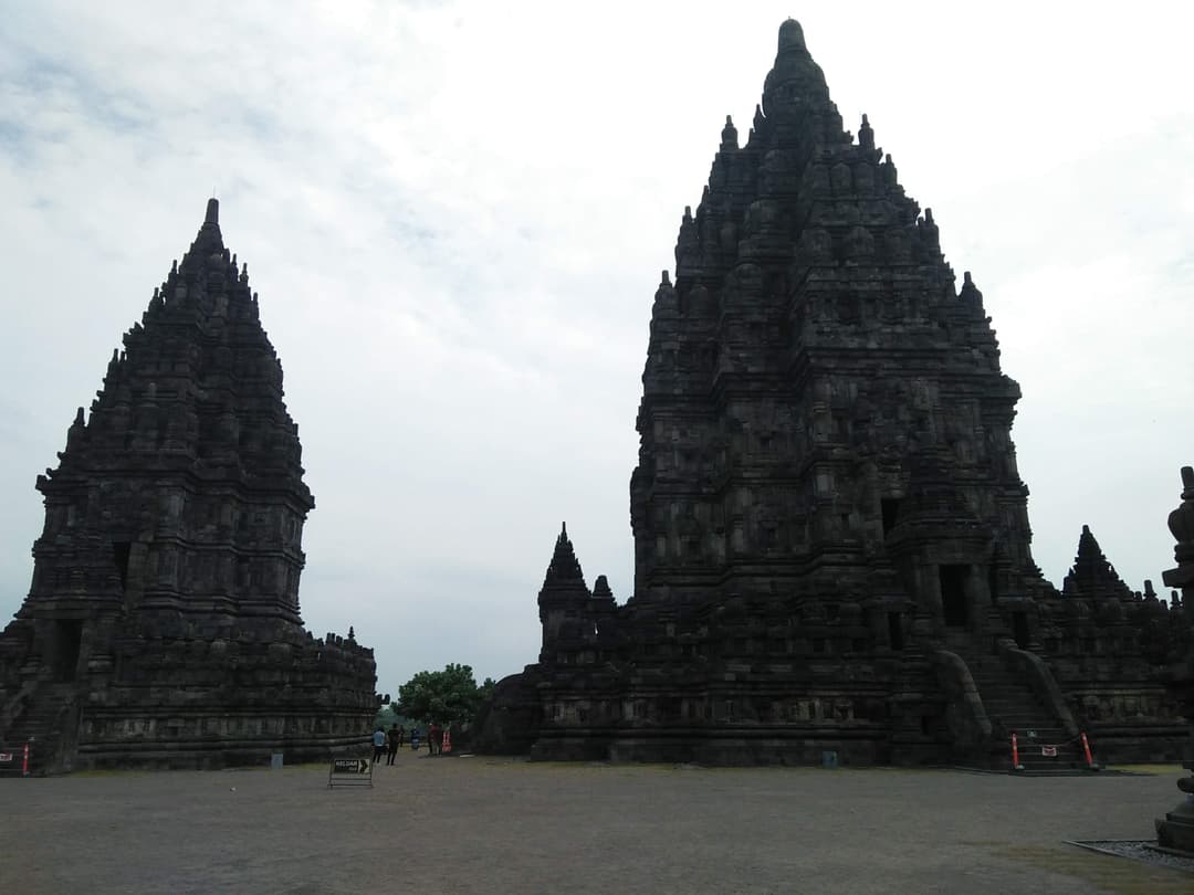 Courtyard view of towering stone temples at Prambanan on an overcast day.
