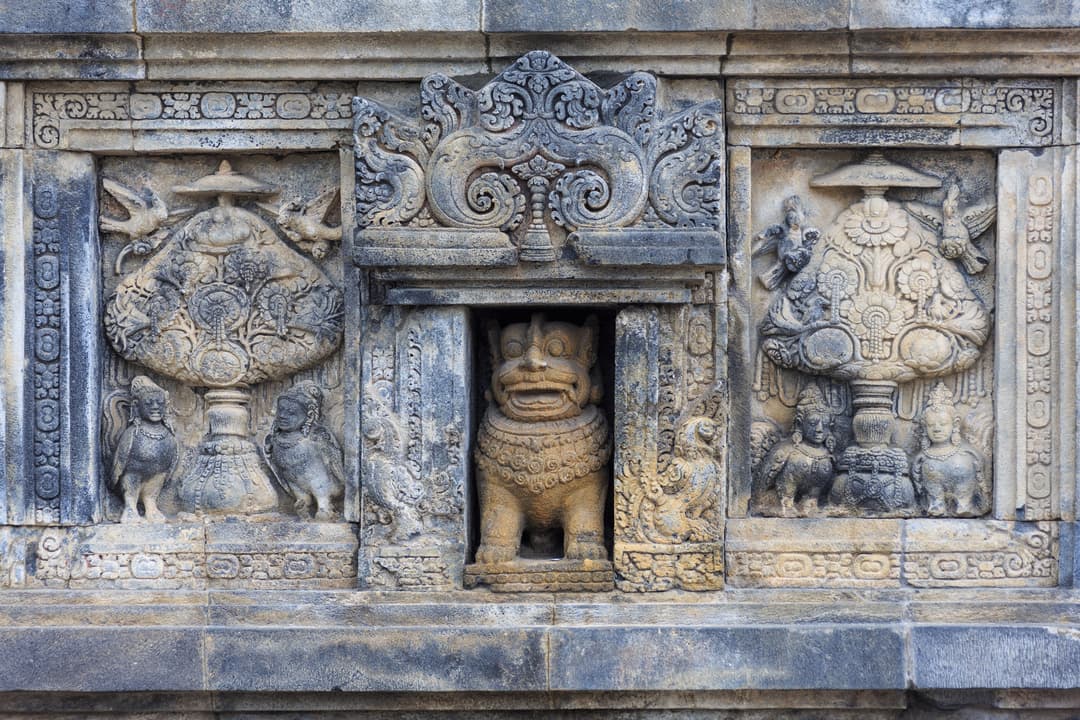 Prambanan Temple relief panel with lion guardian and deities.