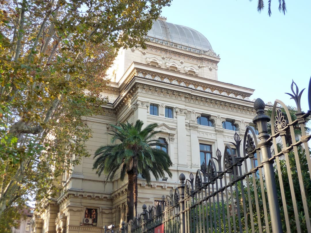 Low-angle exterior view of the Great Synagogue of Rome behind a fence.