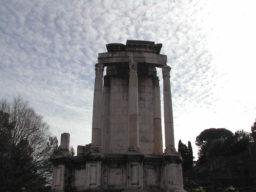 Low-angle view of the partially restored Temple of Vesta under a cloudy sky.