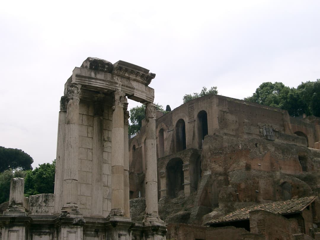 Low-angle view of the Temple of Vesta colonnade with Palatine ruins behind.