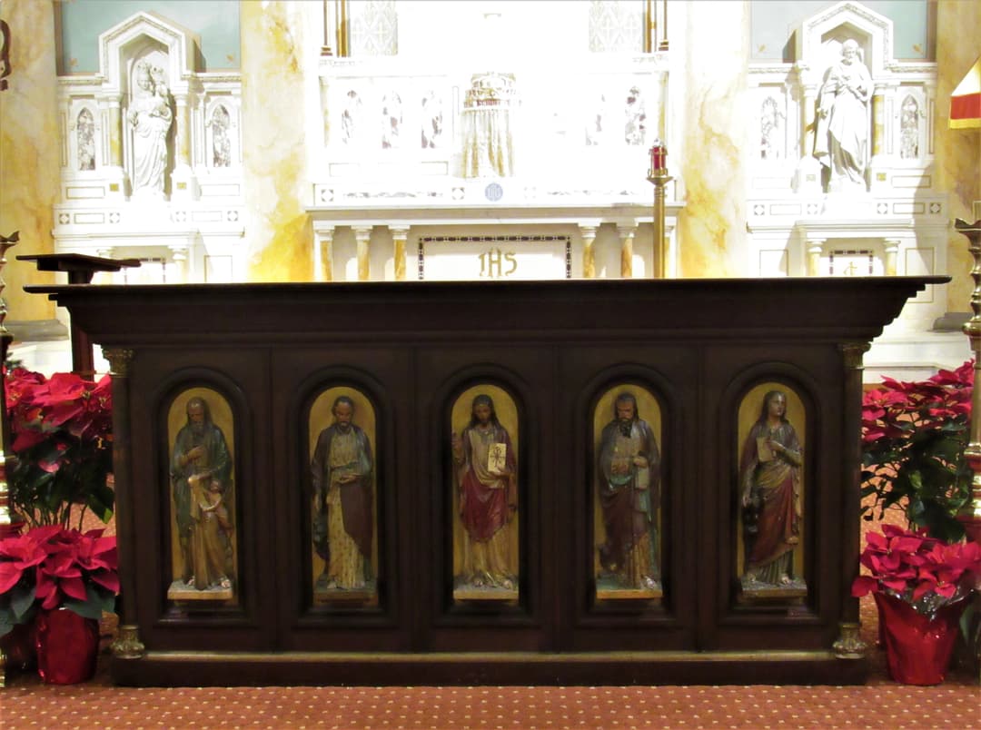 Carved wooden altar featuring Christ and saints, flanked by poinsettias