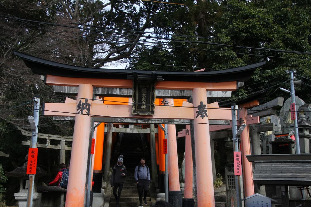 Front view of a large vermilion torii gate over stone steps by day.