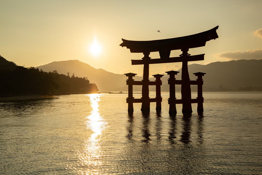 The O-torii gate of Itsukushima Shrine silhouetted at sunset.