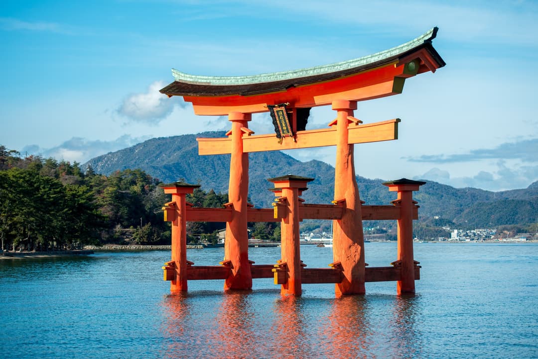 Gerbang O-torii merah terang Kuil Itsukushima yang berdiri di laut, siang hari.
