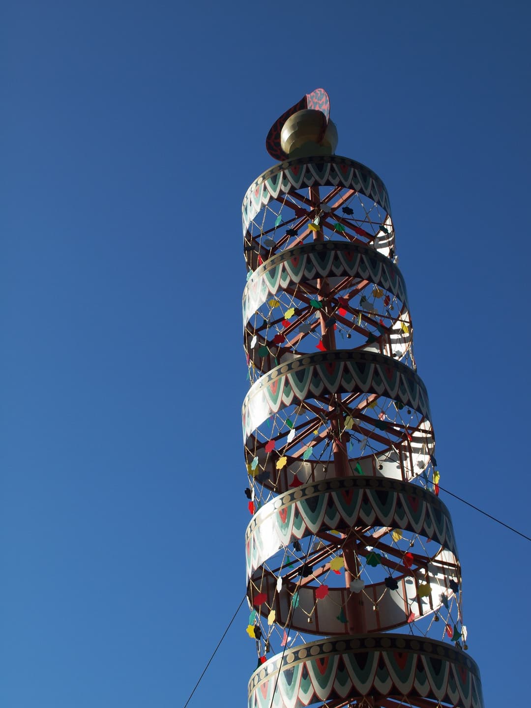 Low-angle view of a decorative ceremonial spire against a clear blue sky.