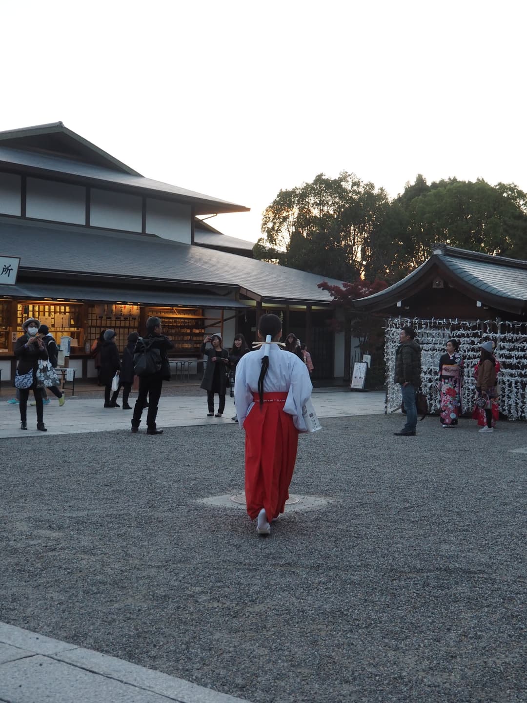 A miko walking across the gravel courtyard at Yasaka Shrine at dusk.
