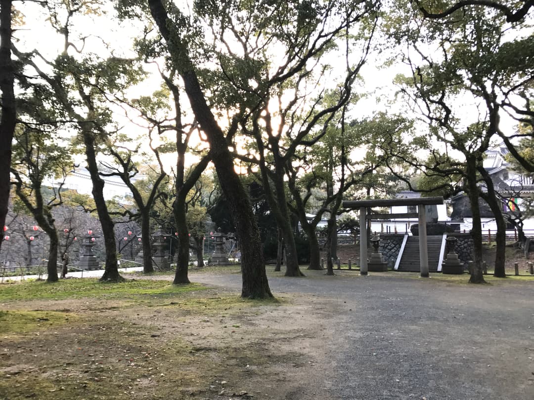 Gravel path through wooded grounds leading to a stone torii gate