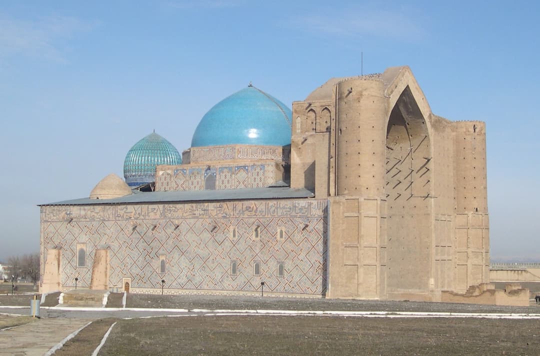 Angled exterior view of the monumental portal and turquoise domes.