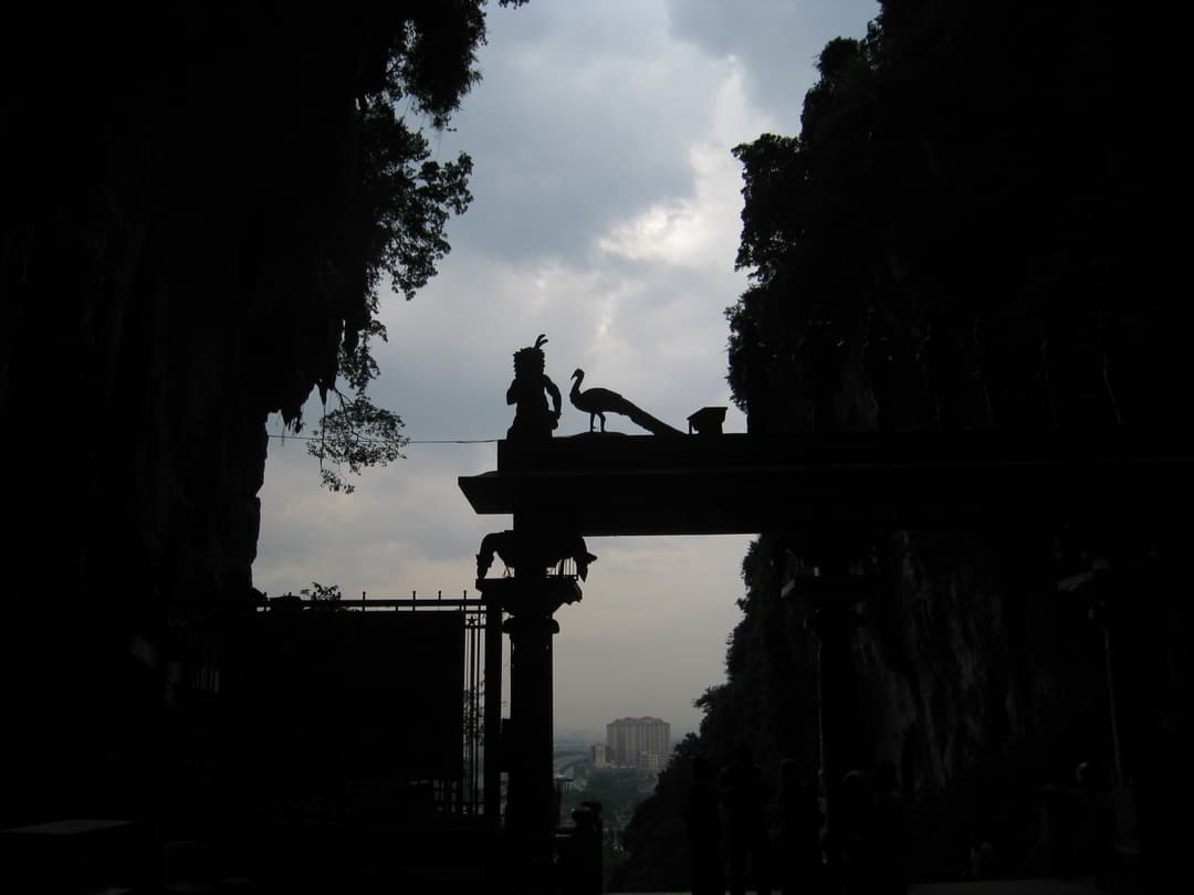 Silhouetted entrance arch with peacock statue framed by cave walls