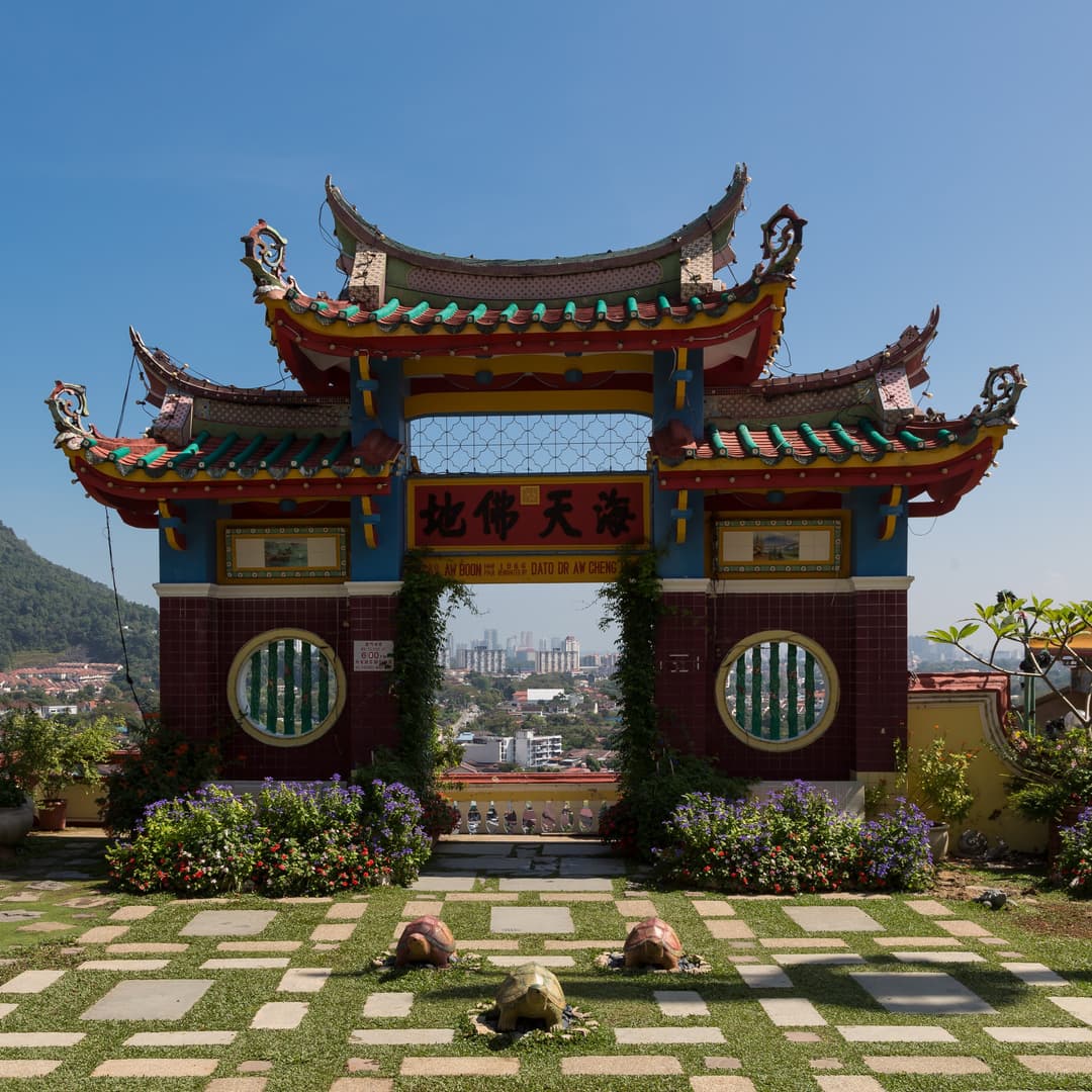 Front view of an ornate Chinese archway and garden overlooking Penang cityscape.