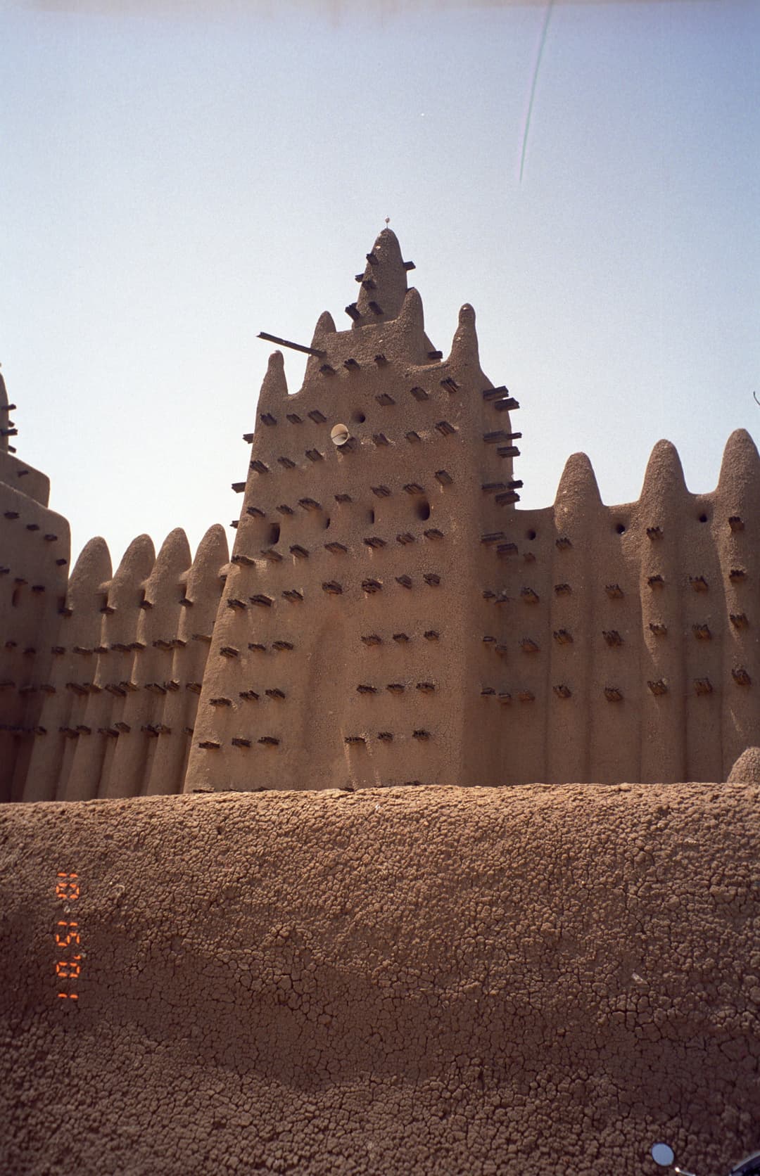 Low-angle view of an earthen minaret tower with projecting timber toron