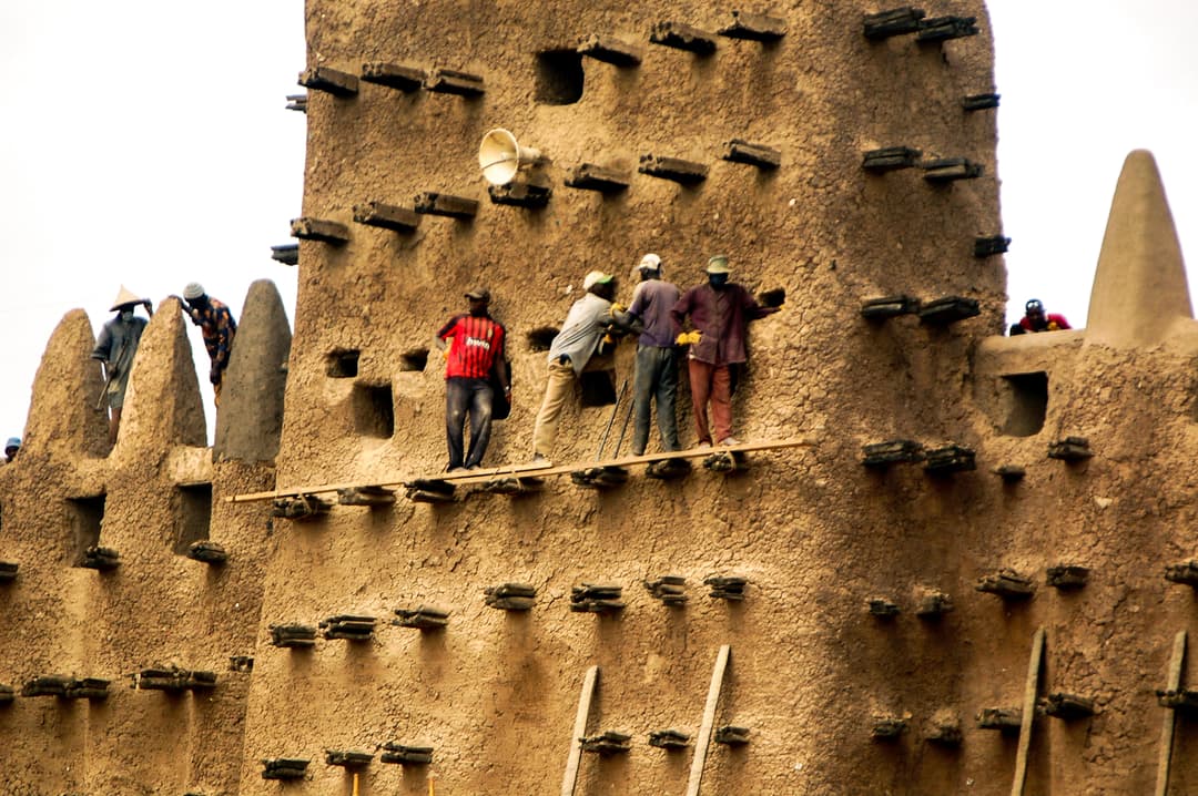 Workers replastering the earthen facade using toron beam scaffolding.
