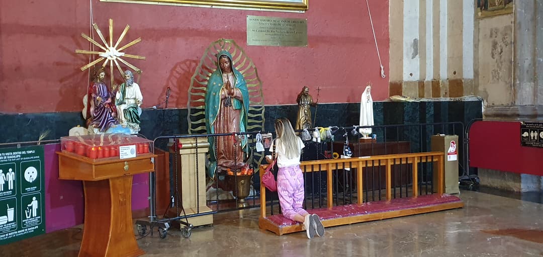 Interior shrine with a devotee kneeling before Our Lady of Guadalupe.