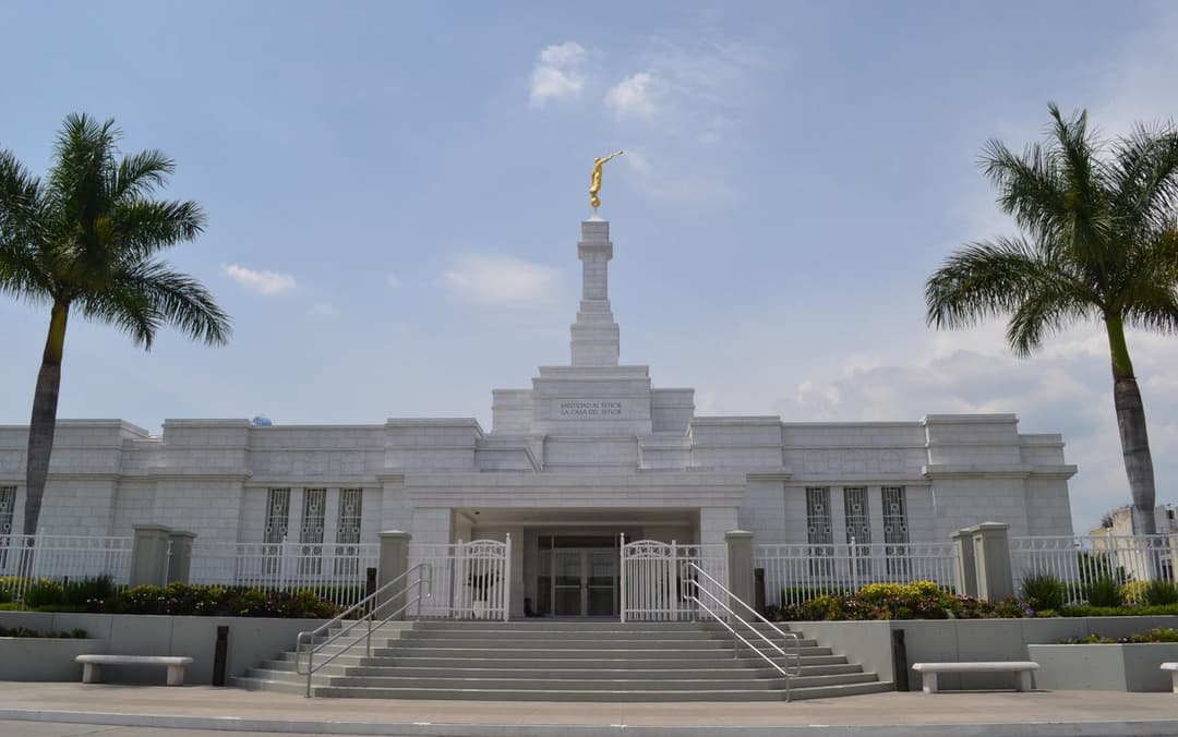 Daytime front view of Guadalajara Mexico Temple with Moroni statue and palm trees.