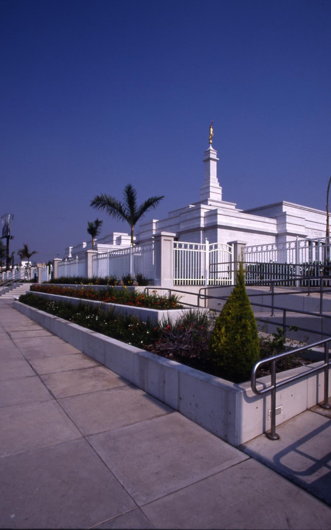 Guadalajara Mexico Temple exterior, golden spire, gardens, and sidewalk.