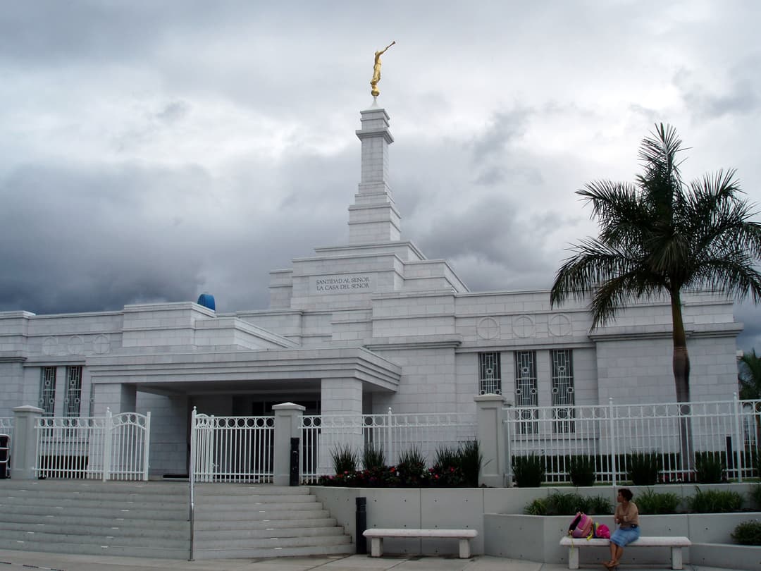 Guadalajara Mexico Temple exterior, Angel Moroni, cloudy sky, woman on bench.