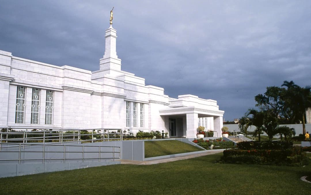 Mérida Mexico Temple exterior, spire with Angel Moroni, gardens, cloudy sky.