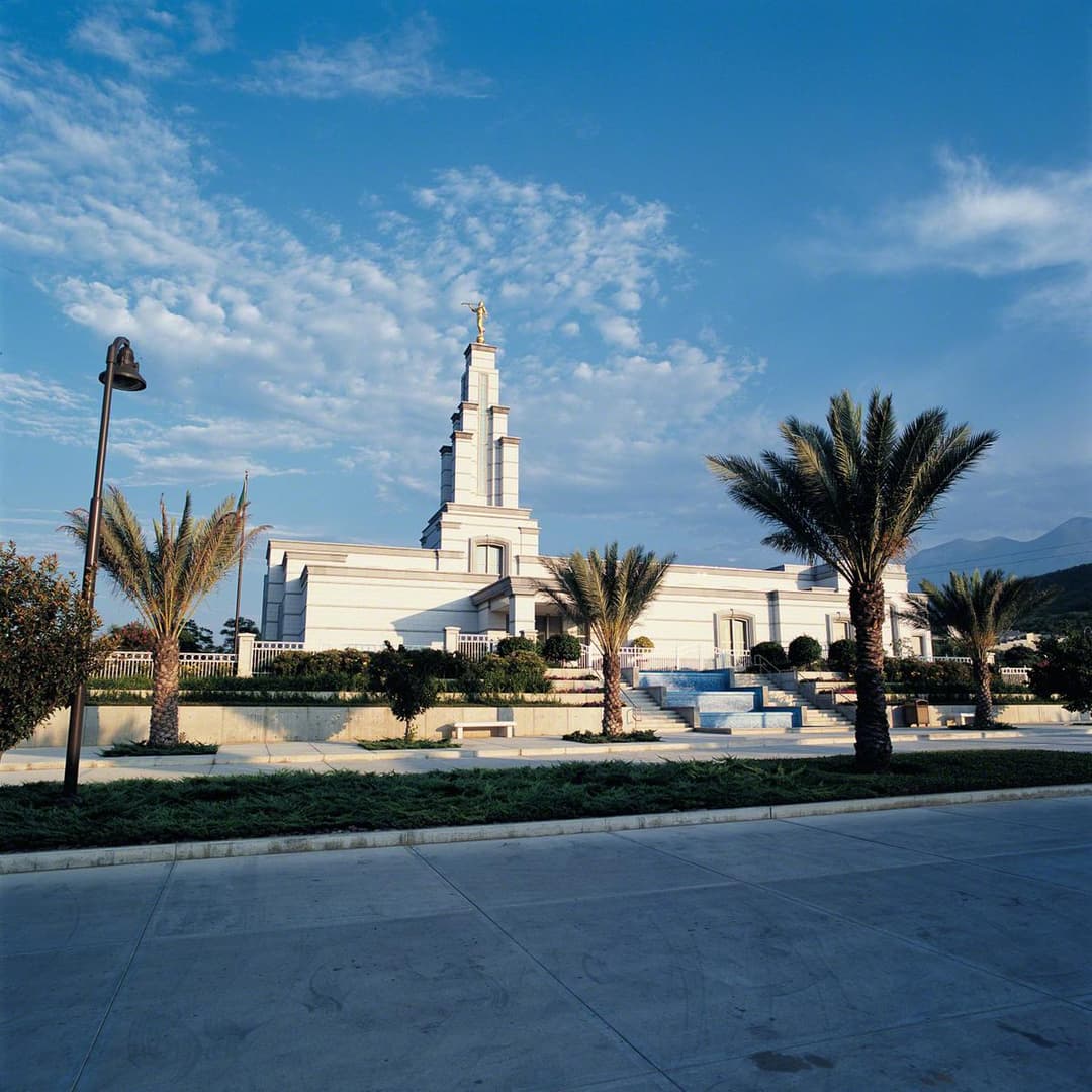 Daytime exterior of Monterrey Mexico Temple with spire and palm trees.