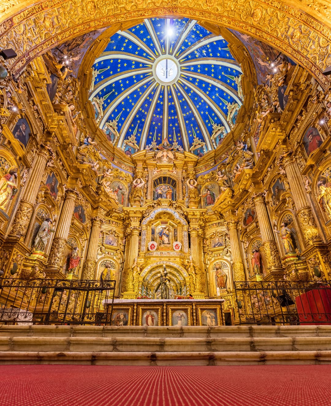 Interior view of the gilded Baroque retablo beneath a starry blue dome.