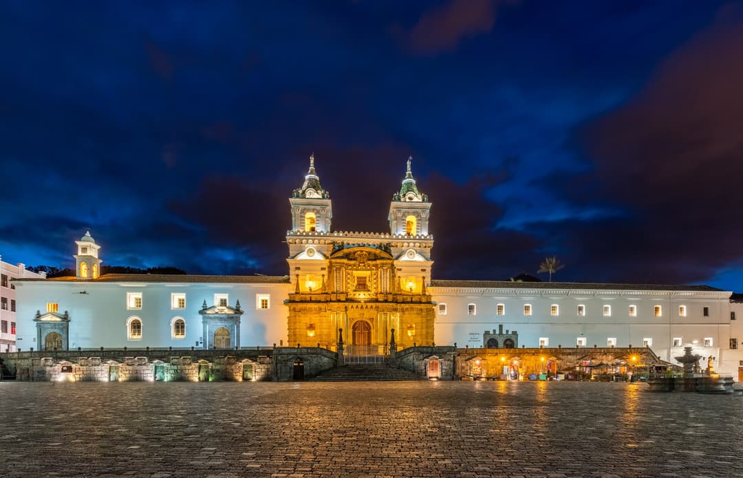 Wide-angle view of the illuminated church facade and plaza at twilight.