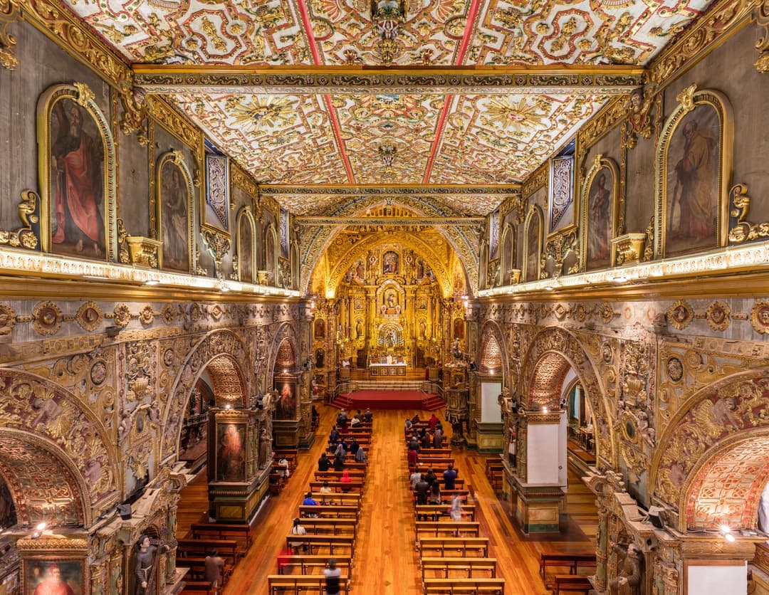 Elevated interior view of the ornate, gilded nave leading to the main altar.