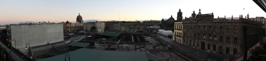 Wide-angle panoramic view of the Templo Mayor archaeological site at dusk.