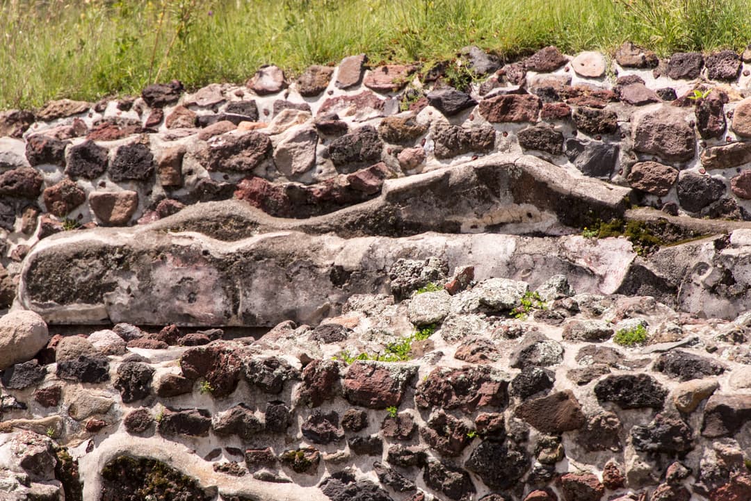 Detail shot of weathered volcanic stone masonry and stucco in direct sunlight.