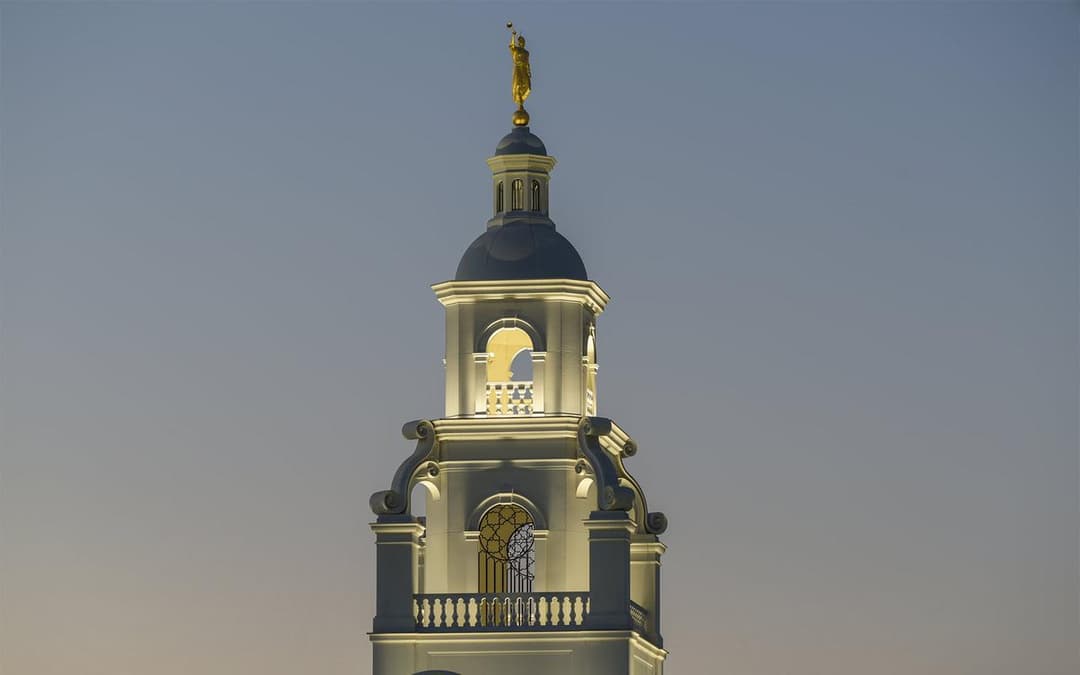 Illuminated multi-tiered tower and Angel Moroni statue at twilight.
