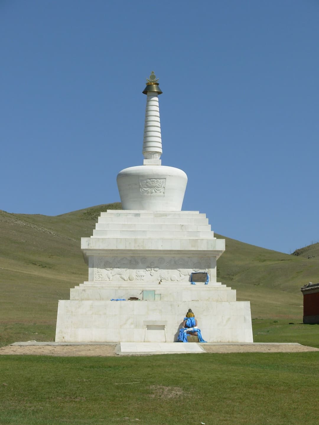 Front view of a white Buddhist stupa against green hills in bright daylight.