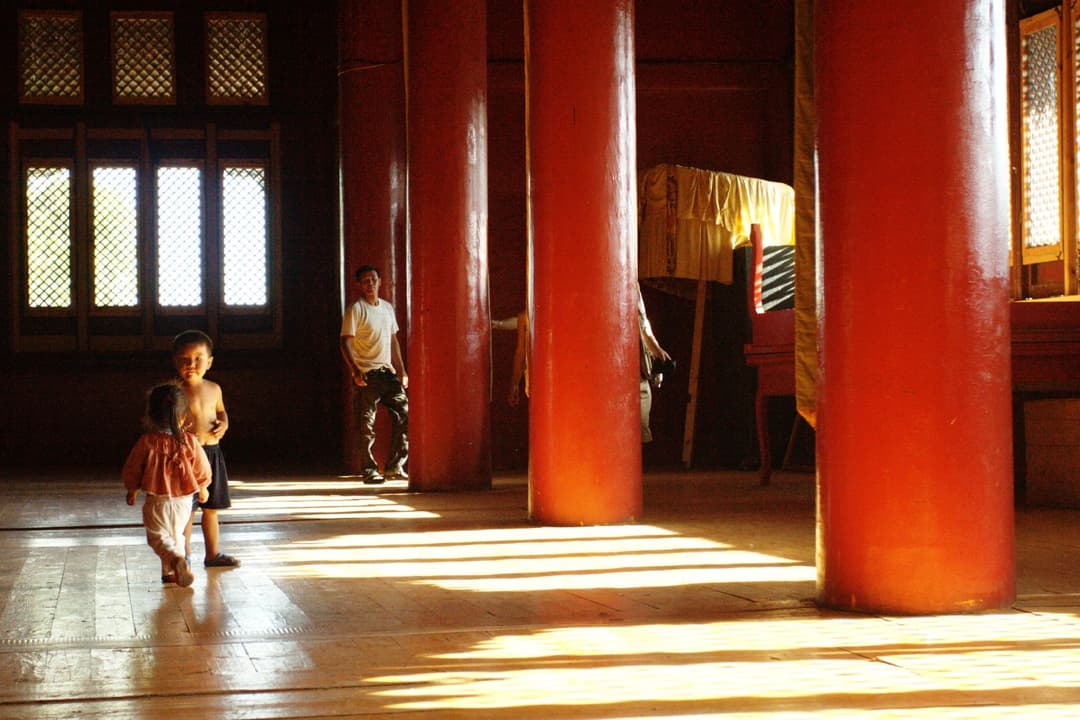 Interior view of a hall with red wooden pillars and streaming sunlight.