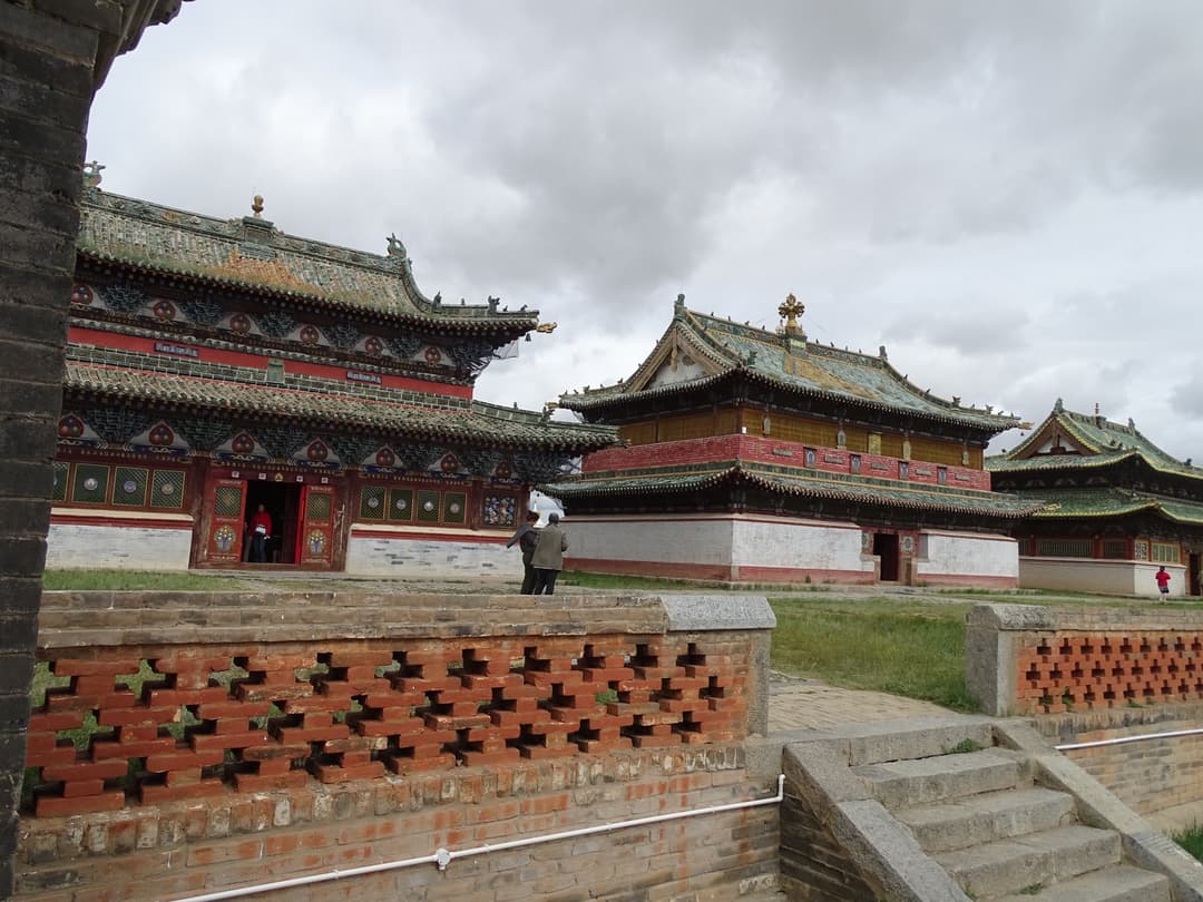 Erdene Zuu Monastery temples viewed from behind a red-brick lattice wall.