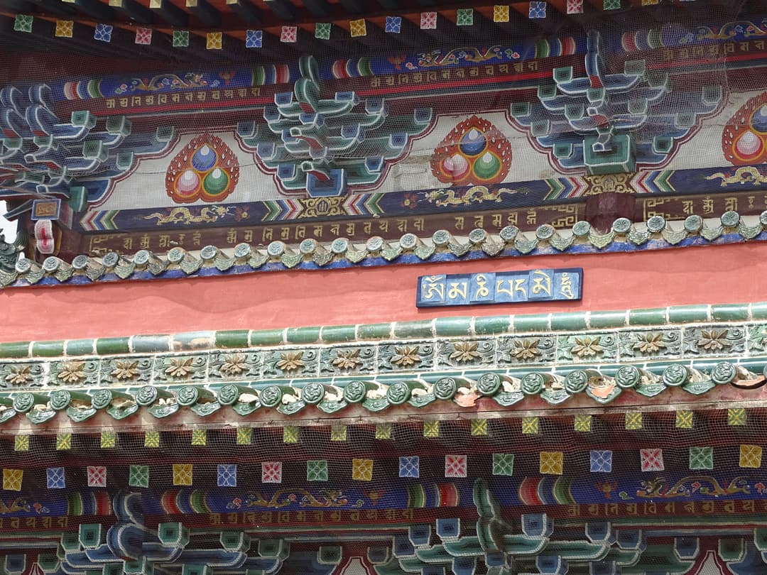Detail of polychrome timber eaves, glazed tiles, and Tibetan mantra plaque.