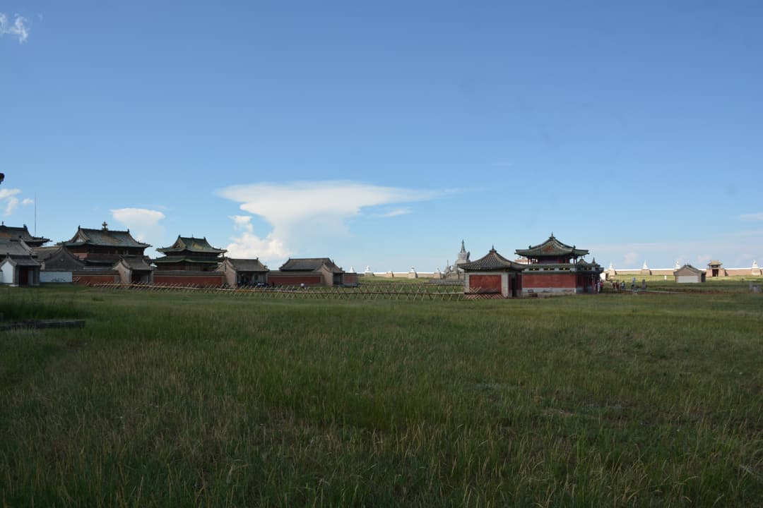 Wide view of Erdene Zuu Monastery temples across an open grassy field.