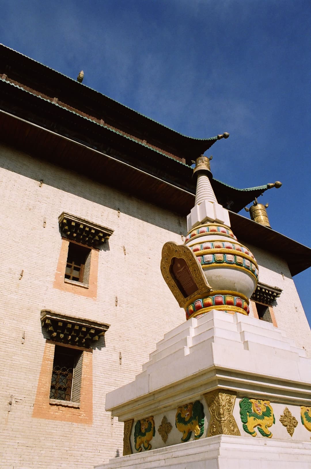 Low-angle view of an ornate stupa before the white facade of Gandan Monastery.