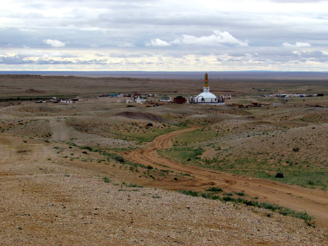 Distant view of a white stupa complex in an expansive desert landscape.