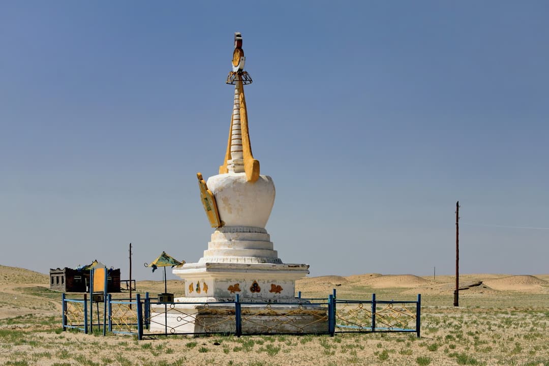 A white Buddhist stupa enclosed by a fence in the arid desert landscape.